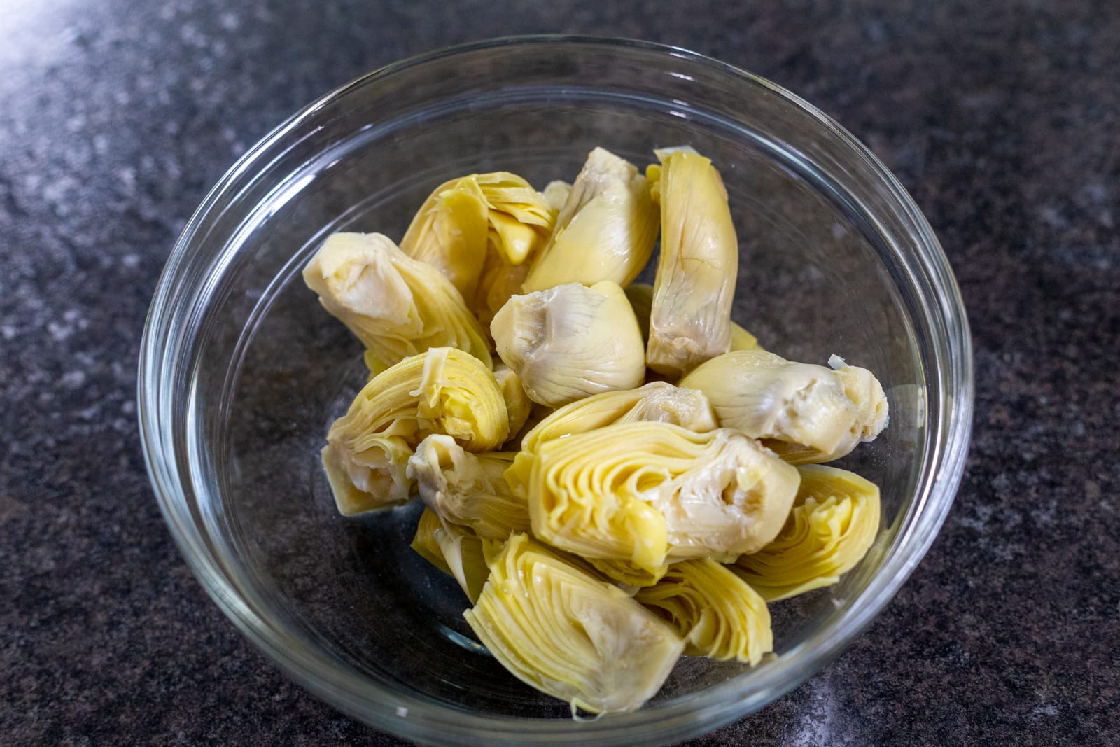 Drained quartered artichoke hearts in a clear glass bowl.