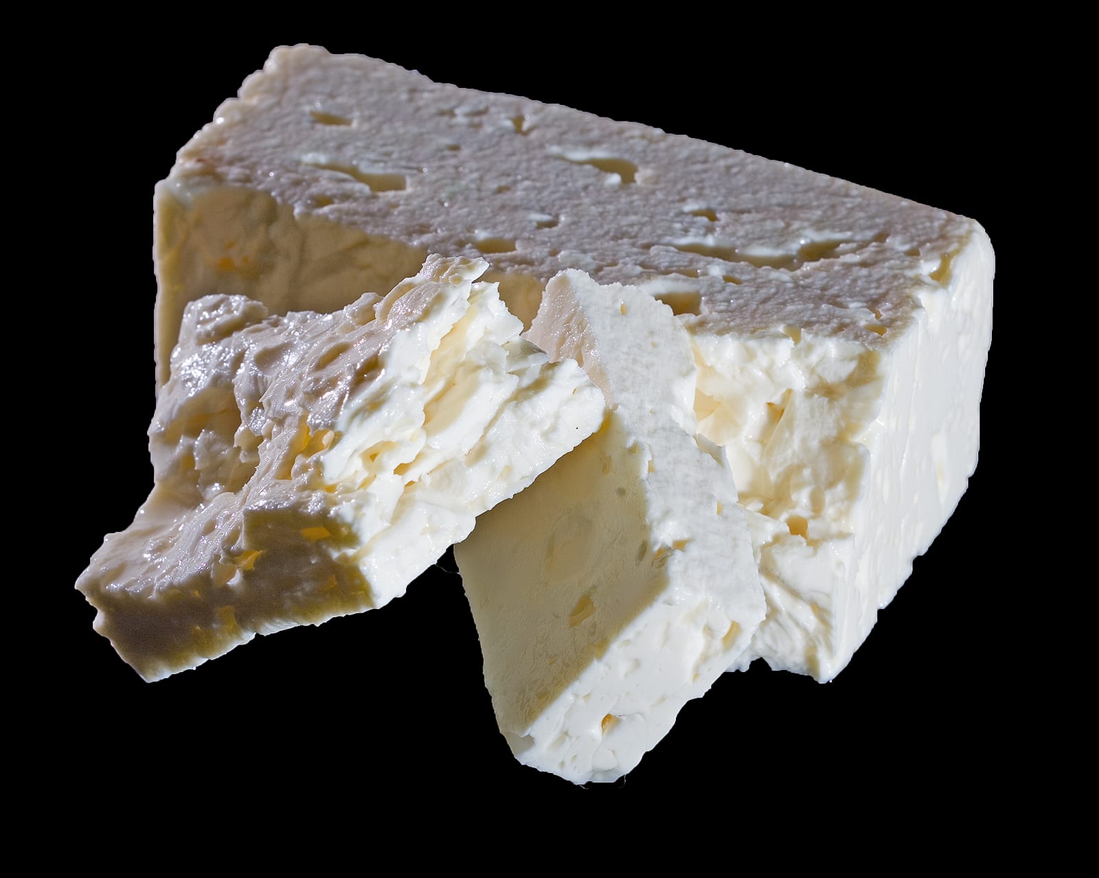 A white block of feta with several rough, creamy shards broken from one corner.