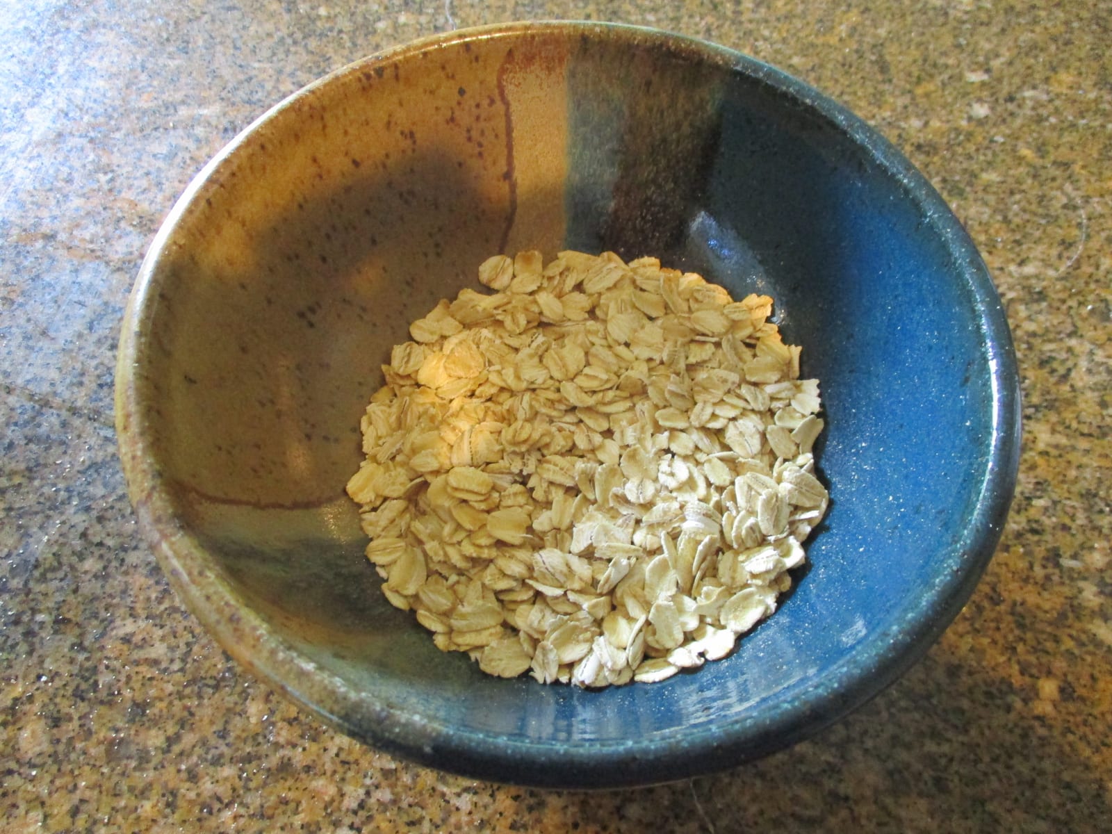Dry rolled oats gathered in a blue-and-brown ceramic bowl.