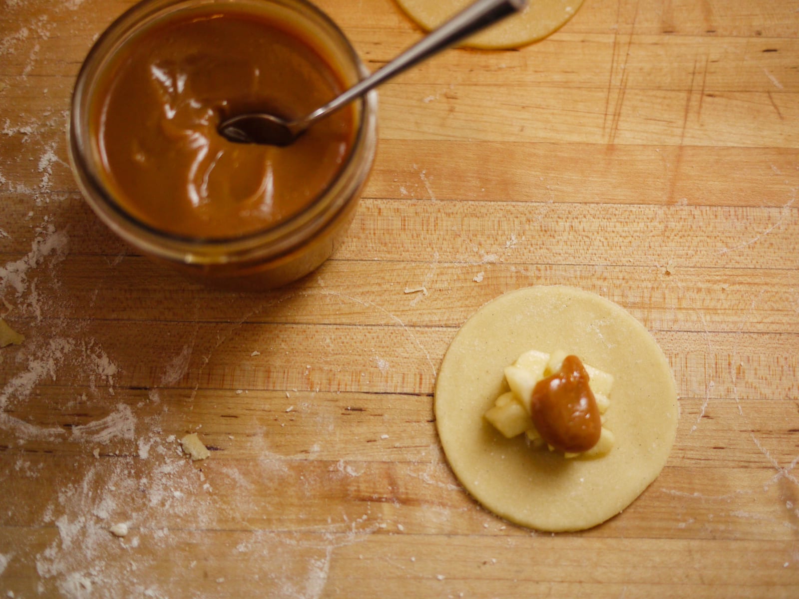 Glossy caramel sauce in a small glass bowl on a floured wooden work surface.