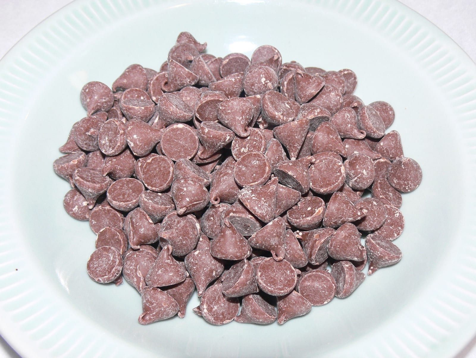 Milk chocolate chips piled on a pale green plate.