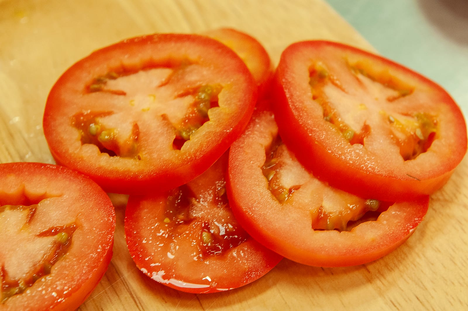 Overlapping red tomato slices glistening on a wooden cutting board.