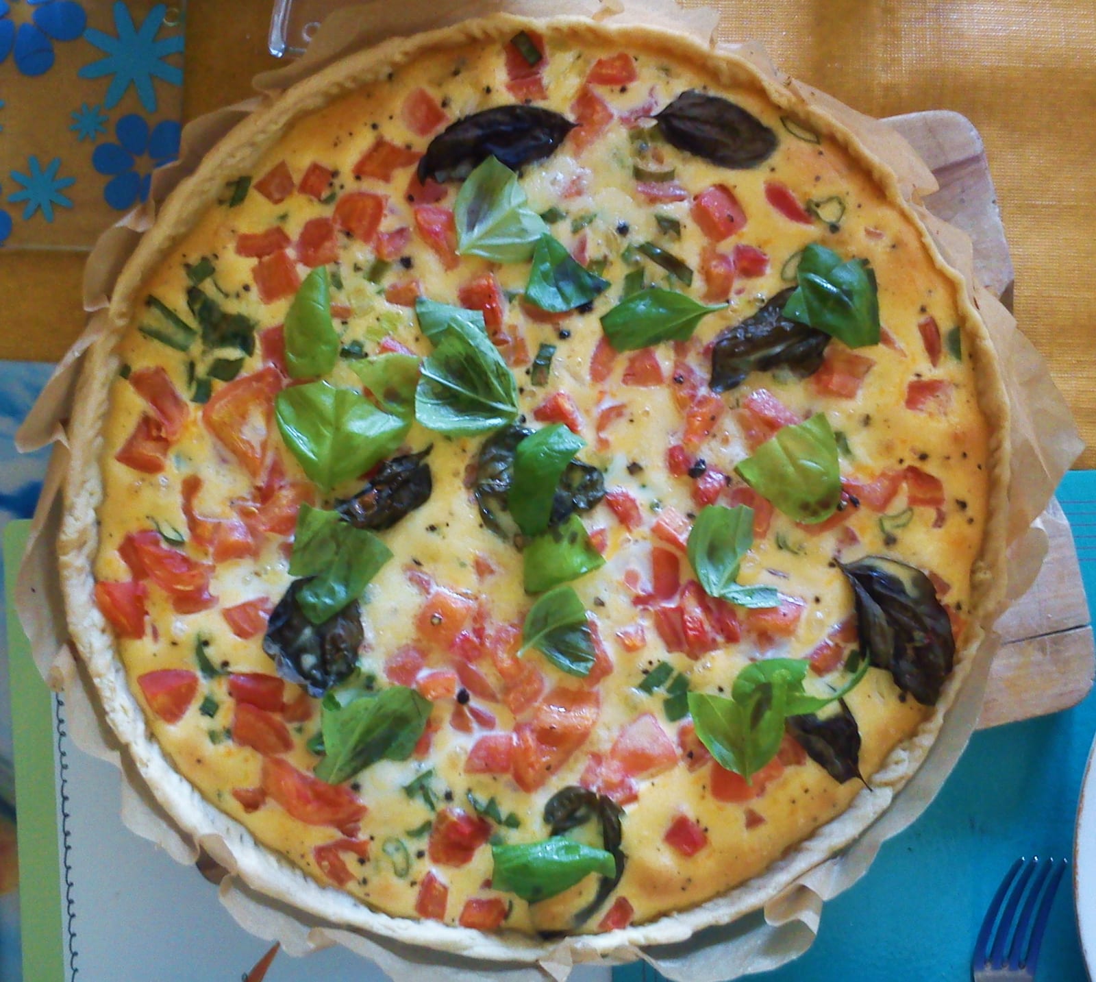 An open tomato and basil tart with a golden filling and a crimped pastry edge.