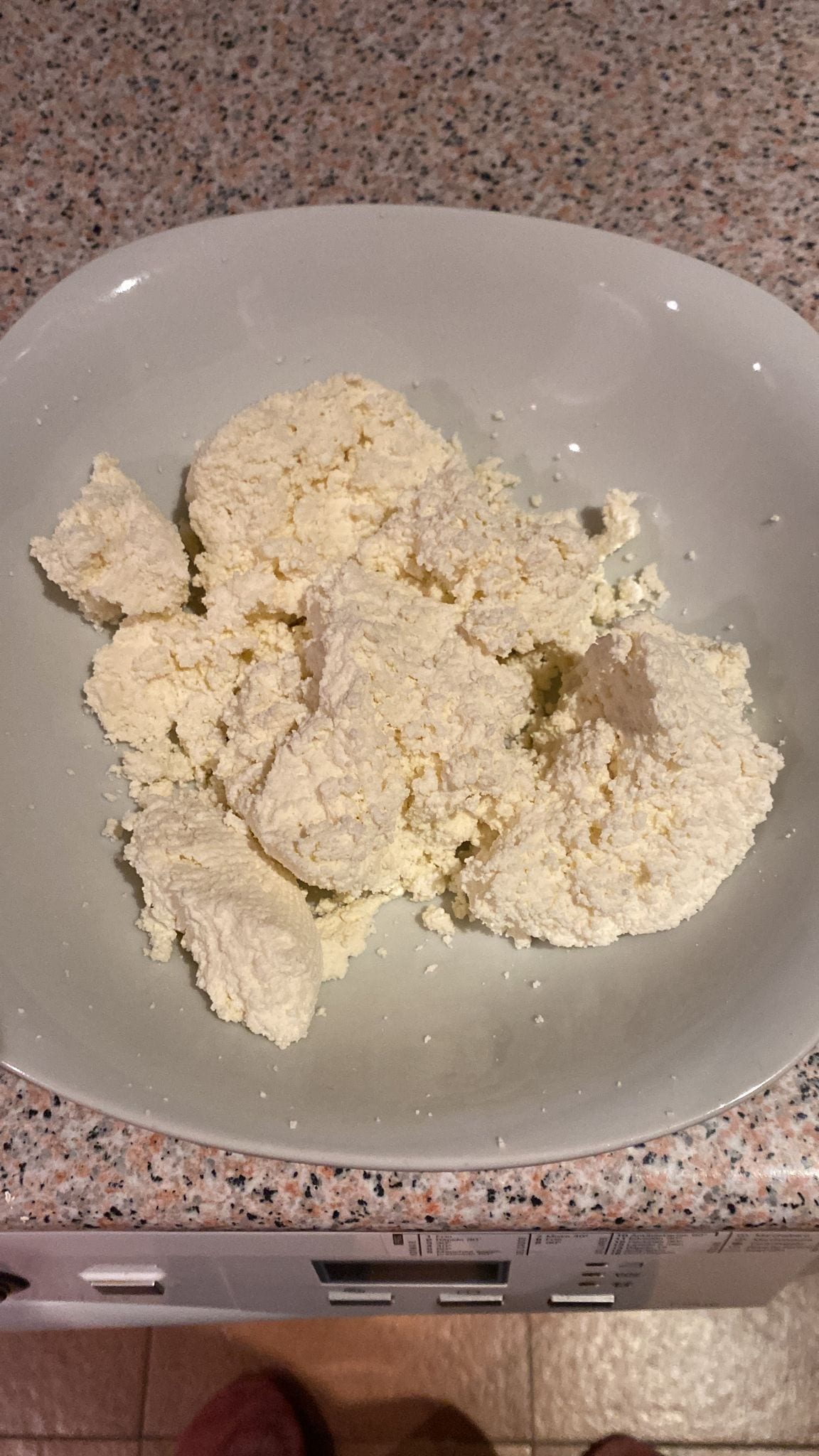 Dry, crumbly homemade tvorog curds on a gray plate.