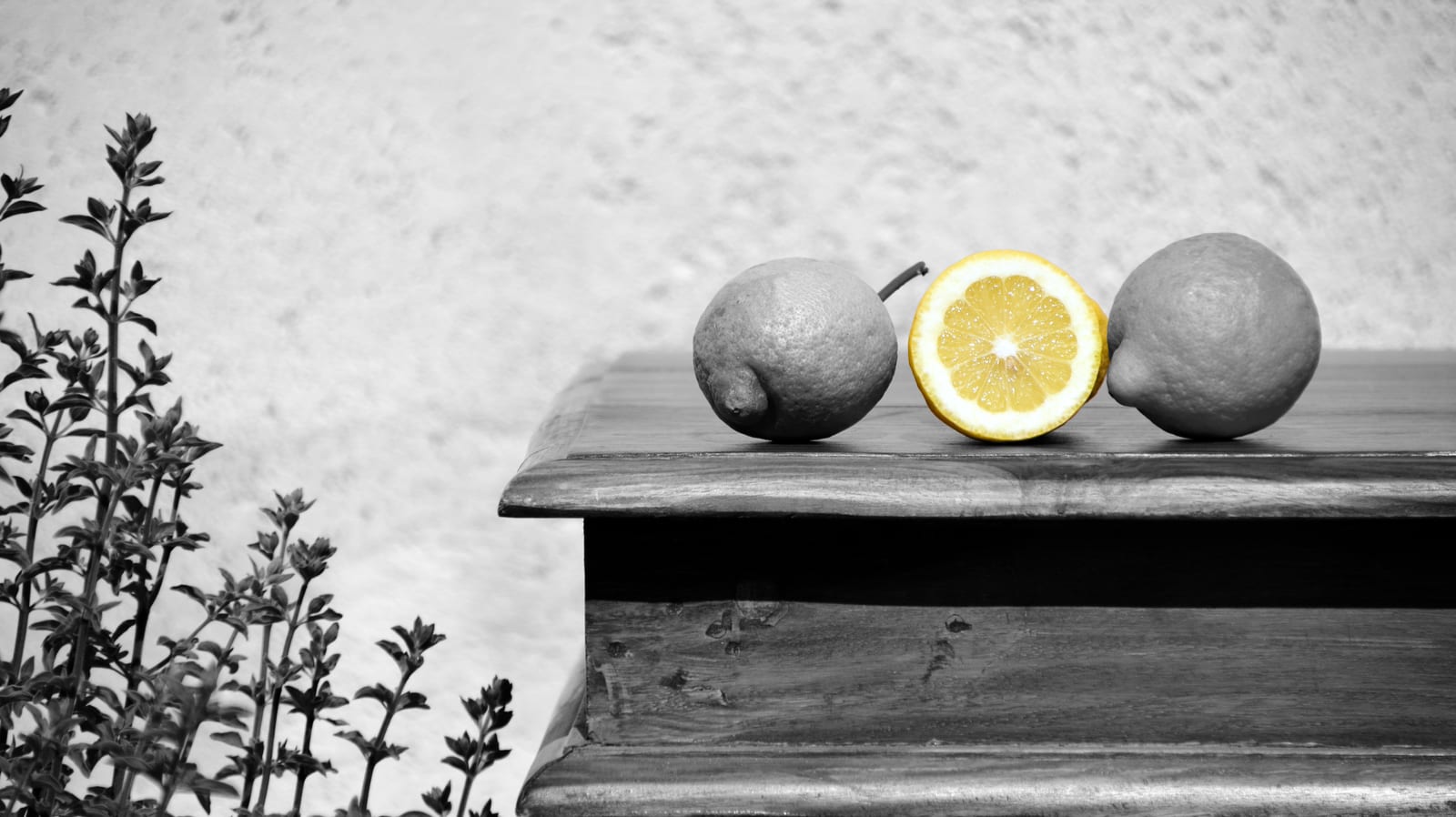 Three lemons on a wooden table rendered in grayscale except for the yellow flesh of the cut lemon.
