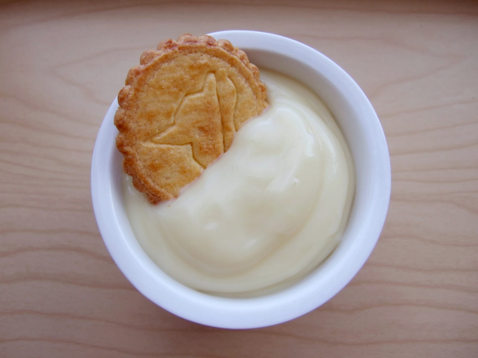 Smooth pale vanilla pudding in a white bowl with a butter cookie.